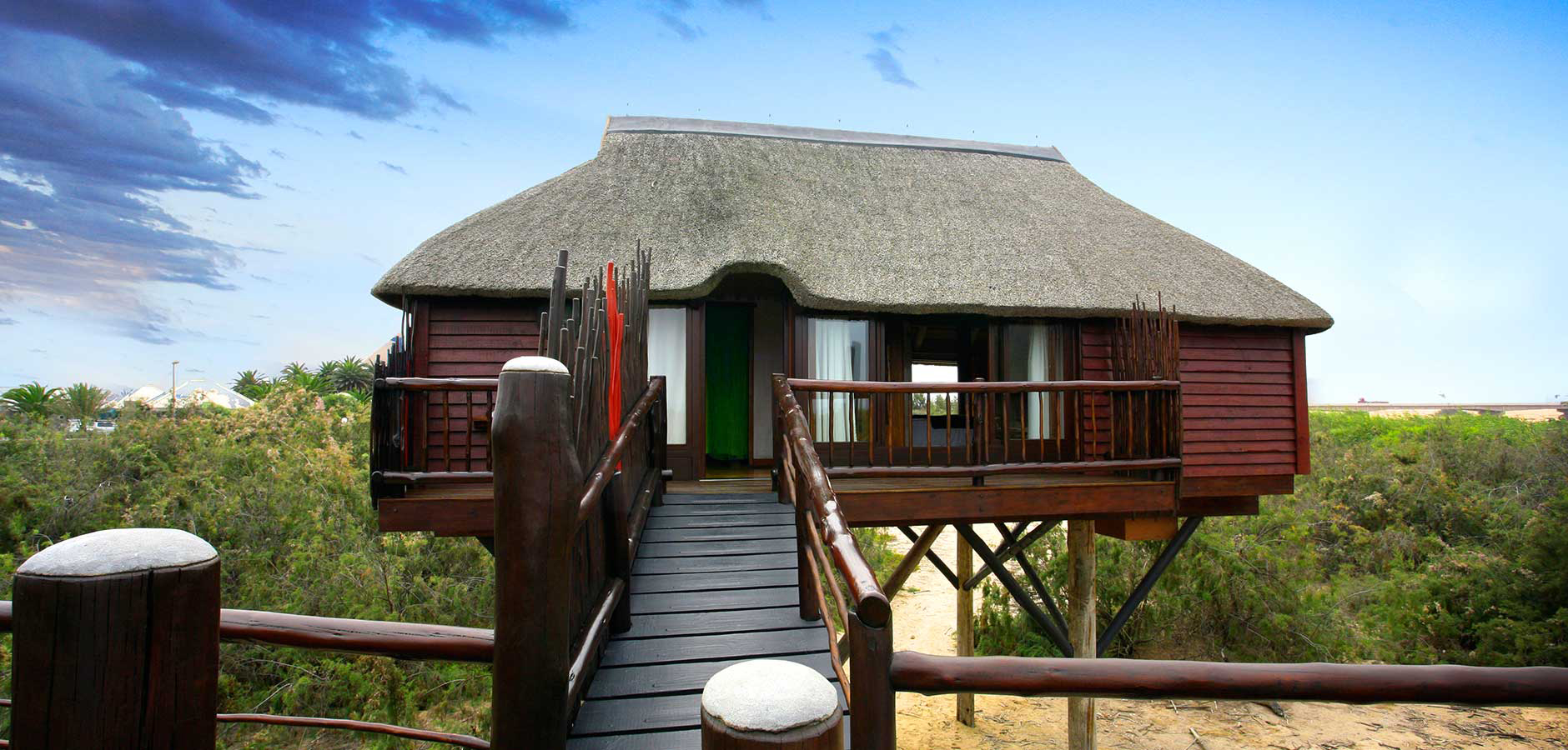 Raised wooden bungalow at The Stiltz, with a thatched roof and timber walkway